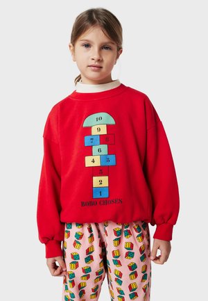 Röd sweatshirt med en hoppa grafik med siffror; kombinerad med rosa mönstrade byxor som visar färgglada tärningsillustrationer.