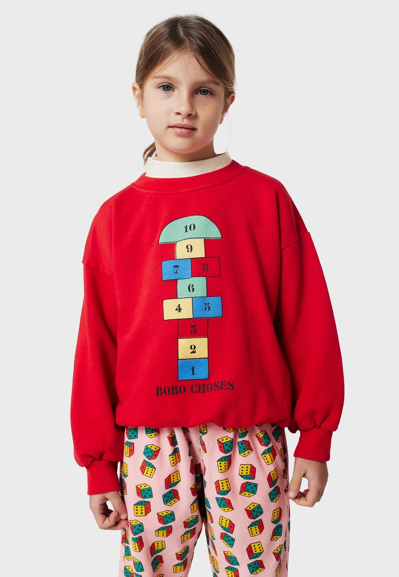 Felpa rossa con una grafica a campana con numeri; abbinata a pantaloni rosa con fantasia che mostrano illustrazioni di dadi colorati.