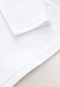 Tissu en coton blanc avec une finition texturée, présentant une manche repliée et des bords lisses. Le tissu semble propre et sans défaut.