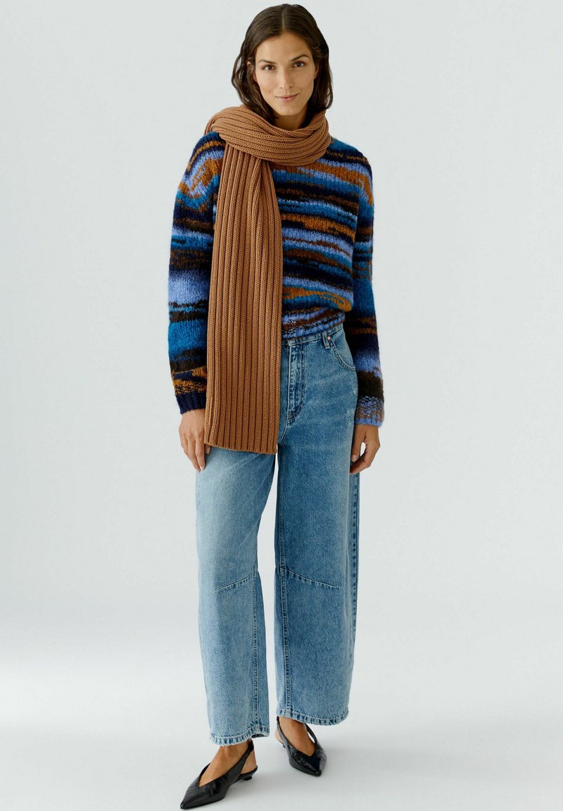 Gestreifter Pullover in Blau, Braun und Orange; kombiniert mit hellblauen, weiten Jeans und einem gerippten braunen Schal. Schwarze spitze Ballerinas.