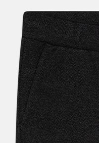 Stoff im schwarzen Fischgrätenmuster zeigt einen Teil einer Hose, die über eine glatte Textur und seitliche Taschedetails verfügt.