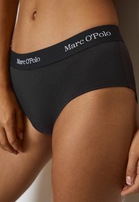 Slips en coton noir avec une large ceinture élastique arborant le logo "Marc O'Polo" en blanc. Texture lisse avec un design ajusté.