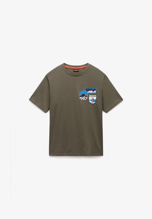 Olive green cotton T-shirt with short sleeves, round neck, featuring embroidered patches in blue and white, including the year "1987."