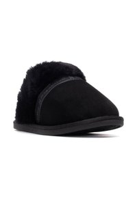 Pantuflas de ante negro con un suave cuello de pelo sintético. Suela plana negra, puntera redonda y marca en relieve en la banda.