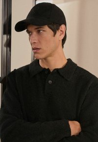 Sort tekstureret fleece skjorte med krave og to knapper; parret med en sort kasket, tilføjer et afslappet, lagdelt look.