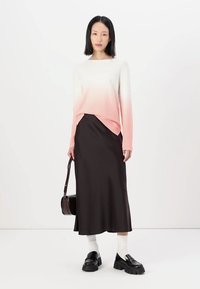 Gebreide trui met een verloop van wit naar lichtroze, gecombineerd met een zwarte satijnen midi-rok. Zwarte platformschoenen en een kleine handtas.