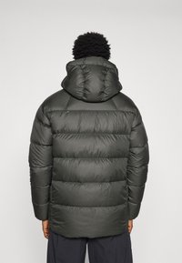 Casaco puffer verde escuro com capuz, apresentando seções acolchoadas e uma textura lisa e brilhante. A vista traseira mostra punhos e bainha canelados.