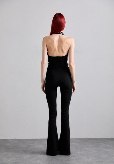 Black jumpsuit with a fitted top and flared legs. Smooth texture, halter neck design, and seam details enhance the overall silhouette.