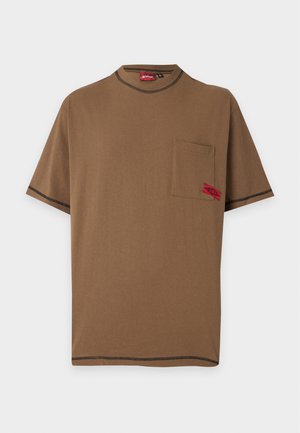 T-shirt marron à manches courtes avec des coutures noires, une poche poitrine sur le côté gauche et une petite étiquette rouge sur la poche.