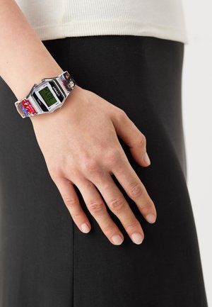 Montre numérique avec un boîtier rectangulaire en argent, présentant un affichage numérique vert et un bracelet à motifs colorés.