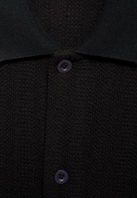 Zwarte gebreide cardigan met een gestructureerde stof, een klassieke kraag en donkerpaarse knopen. Close-upweergave benadrukt de materiaaldetails.