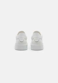 Zapatillas de cuero blanco con un acabado texturizado, puntera redondeada y una gruesa suela de goma blanca. Presentan una pestaña trasera para facilitar el calzado.