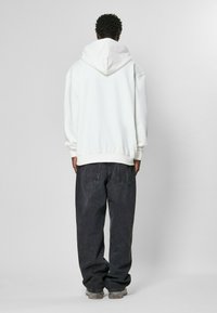 Fehér, oversized kapucnis pulcsi húzózsinórral, laza, sötét farmernadrággal párosítva. Sima felület, minimalista design.