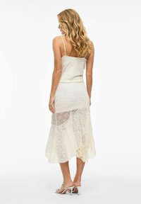 Top cami en satin ivoire avec des fines bretelles, associé à une jupe en dentelle transparente et superposée avec un ourlet asymétrique et un motif texturé.