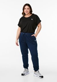Zwarte t-shirt met korte mouwen met een klein logo, gecombineerd met marineblauwe joggerbroeken met een trekkoord en zijzakken, gedragen met grijze sneakers.