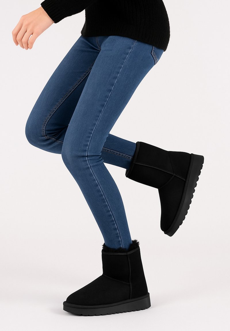 Zwarte suède enkellaarsjes met een zachte bontafwerking, rubberen zool en ronde neus, gedragen met blauwe skinny jeans en een zwarte gebreide trui.