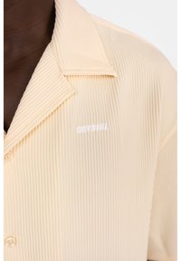 Camisetta corta a maniche corte di un giallo pallido, a costine, con colletto a scollatura e logo "CRYSTAL" ricamato in bianco, dotata di chiusure a bottoni nella parte anteriore.