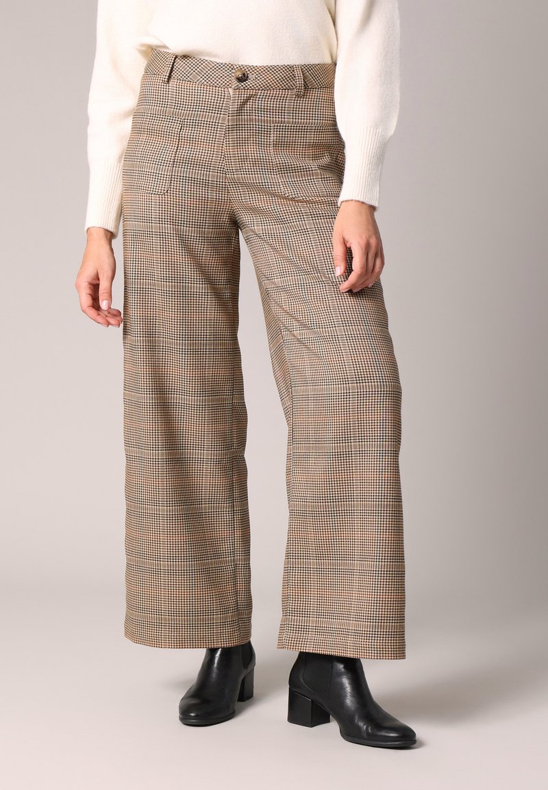 Pantalons à carreaux marron avec une coupe large, taille haute et poches avant, associés à des bottines noires. Texture de tissu lisse.