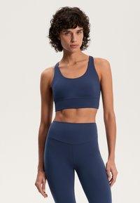 Marinblå sport-bh med rundad halsringning och breda axelband, tillverkad av elastiskt material. Sömlös design som förbättrar komfort och flexibilitet.