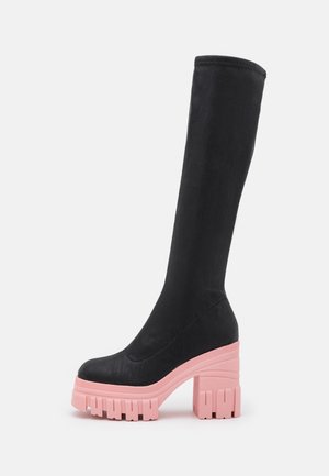 Botte noire montante jusqu'au genou avec une texture lisse et un talon compensé épais rose. Présente un embout arrondi et un design de tige ajustée.