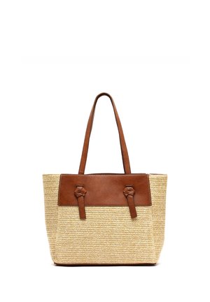 Beżowa pleciona torba typu tote z brązowym skórzanym wykończeniem i długimi brązowymi skórzanymi uchwytami, stojąca pionowo na białym tle.