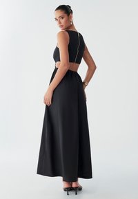 Zwarte tweedelige jurk bestaande uit een crop top met ritssluiting aan de achterkant en een lange, vloeiende rok. Glad materiaal met een uitgesneden detail bij de taille.