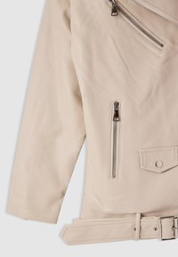 Manica di giacca in pelle beige con tasche con cerniere argento e cintura abbinata con fibbia argento su sfondo chiaro.