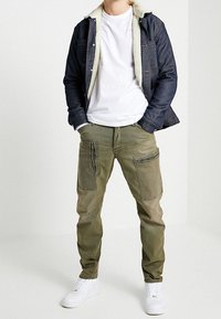 Jeansjacka med fårskinnskrage, vit t-shirt, cargo-byxor i olivgrönt, dragkedjefickor, avslutad med vita sneakers.