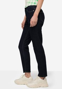 Jeans de mezclilla azul oscuro con un corte ajustado, con costuras amarillas en contraste y cinco bolsillos. Combinados con zapatillas de color claro.