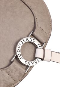 Borsa a tracolla beige con texture e con un accento in metallo argentato di forma circolare. Presenta una tracolla crema e dettagli del logo del marchio sull'anello in metallo.