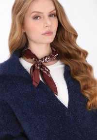 Navyblauwe, pluizige cardigan met twee knopen en een reverskraag, gecombineerd met een bordeauxkleurige zijden sjaal met patroon die om de hals is geknoopt.