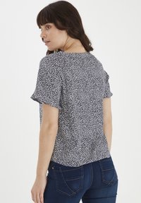 Top a maniche corte in navy con un motivo a spruzzi bianchi. Fit casual, scollatura rotonda e tessuto morbido al tatto. Abbinato a jeans blu scuro.