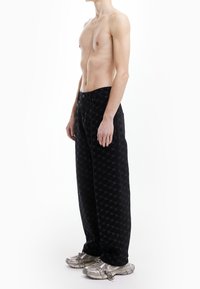 Pantalon noir à motifs, coupe ample, en tissu doux avec un design discret de logo. Associé à des baskets métalliques.