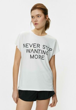 Hvid kortærmet T-shirt i let stof med sort tekst "NEVER STOP WANTING MORE" hen over fronten, med en afslappet pasform.