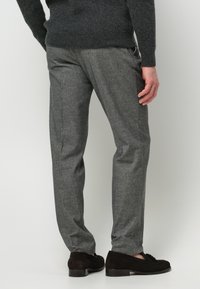 Graue Wollanzughose mit geradem Schnitt; dezente Textur und seitliche Taschen; kombiniert mit dunkelbraunen Wildlederschuhen. Keine sichtbaren Verzierungen.