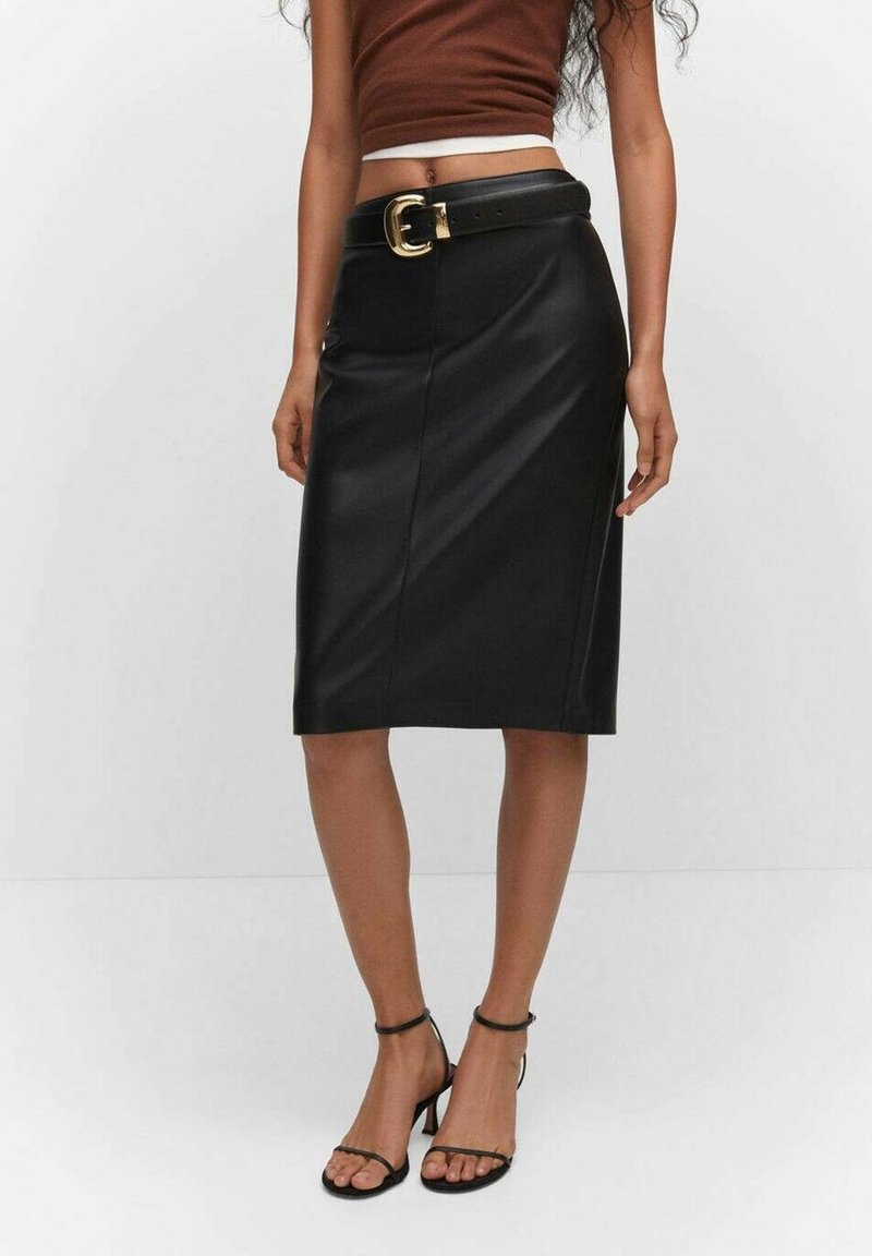 Femme portant une jupe en cuir noire longueur genou avec une ceinture noire à boucle dorée, un top court marron et des talons noirs à lanières.