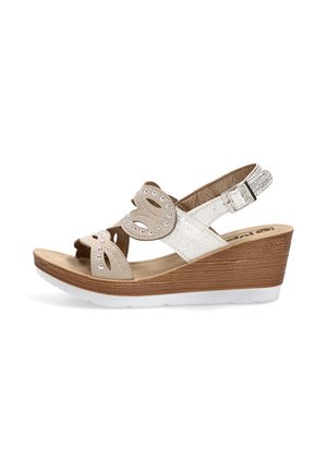Sandalia cuña beige y blanca con recortes decorativos, tachuelas plateadas, pulsera en el tobillo con hebilla y suela de plataforma con textura de madera.