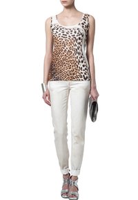 Top sin mangas con estampado animal en beige y marrón, combinado con jeans blancos. Tacones metálicos plateados y accesorios añaden contraste al conjunto.