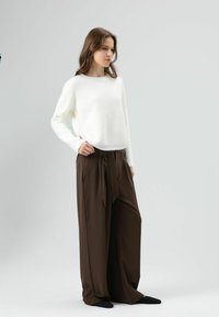 Een wit gebreide trui met een ronde hals en knopen aan de zijkant, gecombineerd met losse, bruine broek met hoge taille en een strikceintuur.