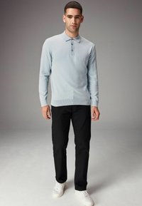 Lyseblå langærmet polo med tre knapper, parret med sorte bukser og hvide sneakers. Glat tekstur, slim fit design.