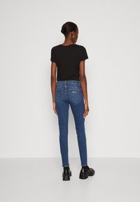 Camiseta negra de manga corta combinada con jeans ajustados azules que cuentan con bolsillos traseros. El modelo lleva zapatos de plataforma negros. Diseño simple y ajustado.