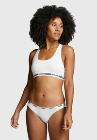 Weißer Sport-BH und passender Bikini mit schwarzen Puma-Logo-Bändern. Glattes Material, sportliches Design, mittlere Breite der Träger und tiefer Schnitt.
