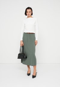 Λευκό μακρυμάνικο τοπ, midi φούστα σκούρου πράσινου με ζώνη στη μέση, μαύρη τσάντα με κοντές λαβές και μαύρα ψηλά τακούνια με μυτερή μύτη.