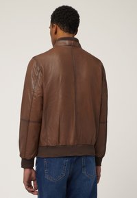 Braune Lederjacke mit geripptem Kragen und Bündchen, ausgestattet mit einer glatten Textur und kontrastierenden Nähten, entworfen mit einer taillierten Silhouette.
