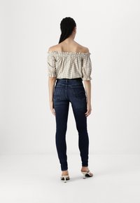 Mörkblå skinny jeans med hög midja, kombinerat med en off-the-shoulder, gräddfärgad blus med ett lätt blommönster och volangärmar.