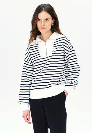 Sweat-shirt rayé avec un motif blanc et marine, col zippé quart, et poignets côtelés, associé à un pantalon noir. Texture de tissu lisse.