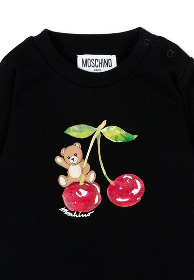 T-shirt bébé noir avec un ours en peluche tenant des tiges de cerises vertes attachées à deux cerises rouges et une étiquette de marque Moschino.