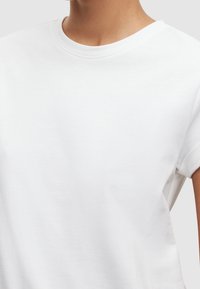 Biała koszulka T-shirt z krótkim rękawem i okrągłym dekoltem, wykonana z gładkiej mieszanki bawełny, charakteryzująca się luźnym krojem i minimalistycznym wzornictwem.