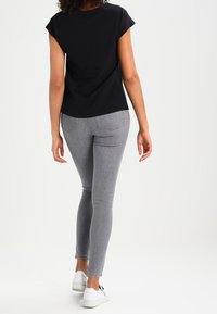 Camiseta negra de manga corta combinada con jeans ajustados grises y zapatillas blancas, mostrando un look casual con una textura suave y una forma ajustada.