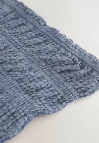 Tissu texturé bleu avec un motif tissé, présentant un bord festonné. Le matériau semble doux et légèrement surélevé par endroits.
